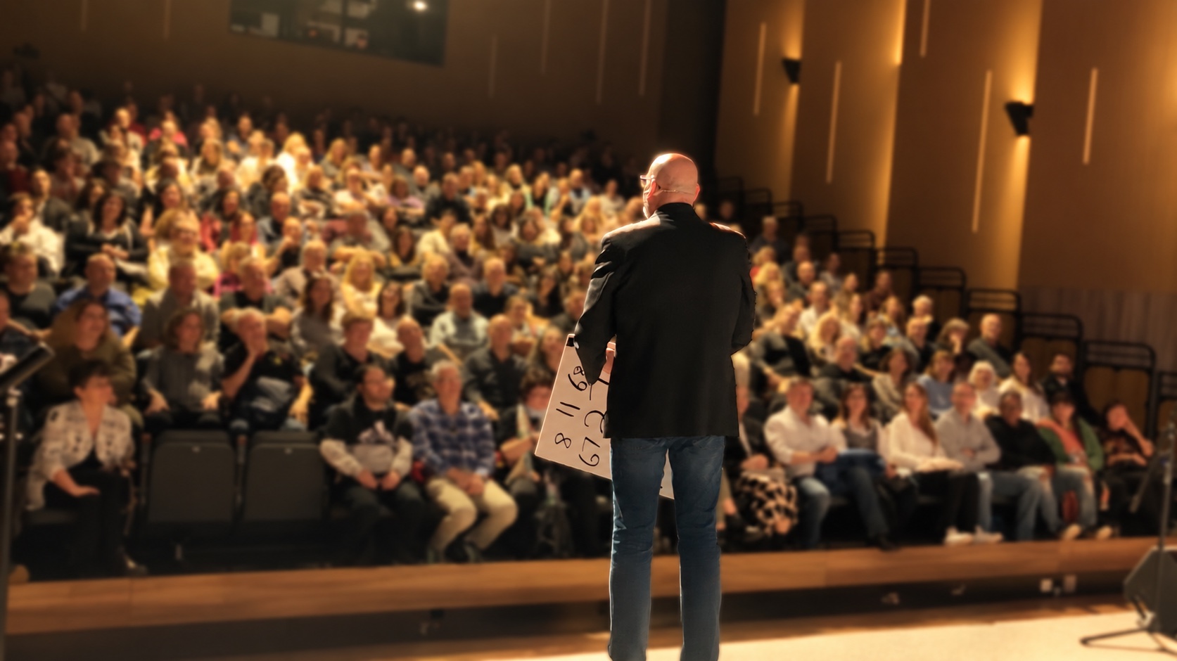 Haim Goldenberg on stage, facing a seated auditorium audience